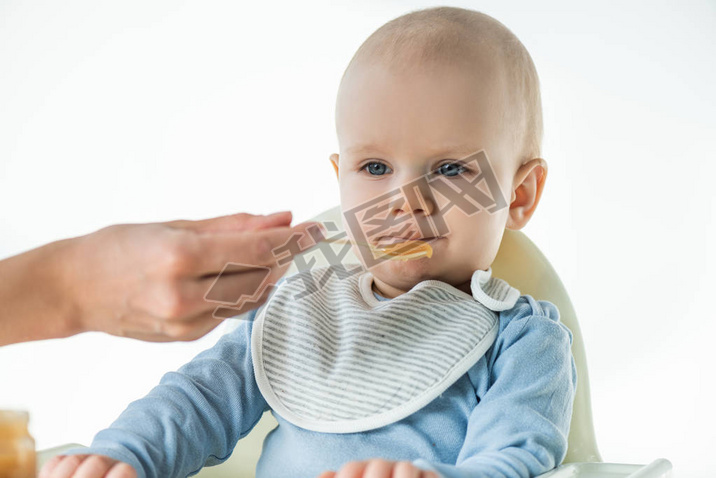 Selective focus of mom feeding adorable baby boy with fruit baby nutrition isolated on white