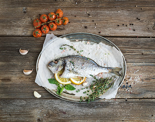 Roasted dorado or sea bream fish with vegetables, herbs and spices on silver tray over rustic wood b