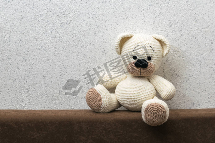 Knitted polar bear with brown paws on the sofa against the wall.