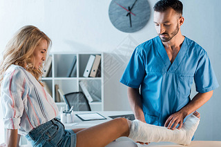 handsome orthopedist looking at fractured leg of woman