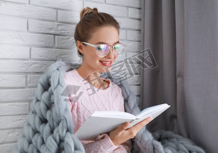 Young woman wearing knitted sweater with book at home