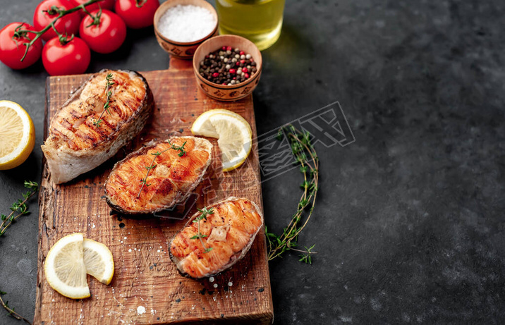 Three grilled salmon steaks with spices, lemon and tomatoes on a stone background