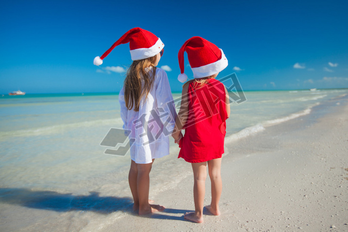 Back view of Little cute girls?in Christmas hats on the exotic beach