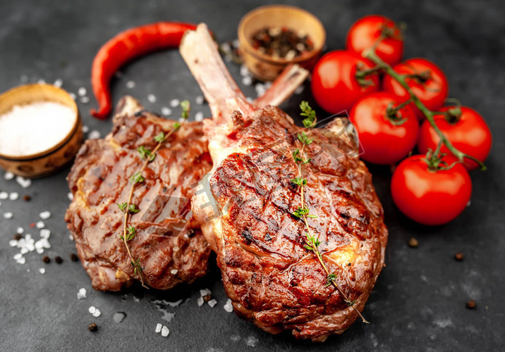 grilled beef steaks - tomahawk with tomatoes and red pepper on a stone background