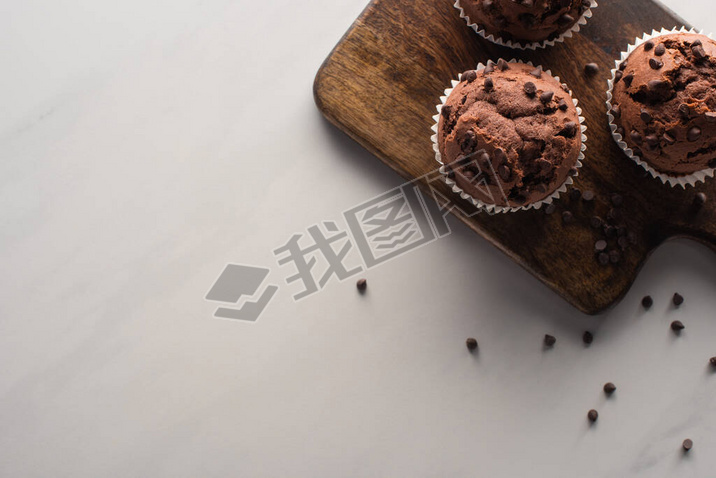 top view of fresh chocolate muffins on wooden cutting board on marble surface