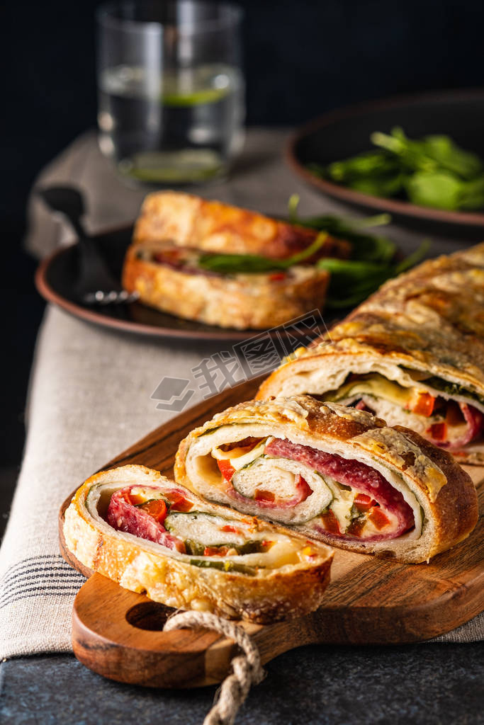 Traditional Italian Stromboli stuffed with cheese, salami, red pepper and spinach. Photo in a dark s