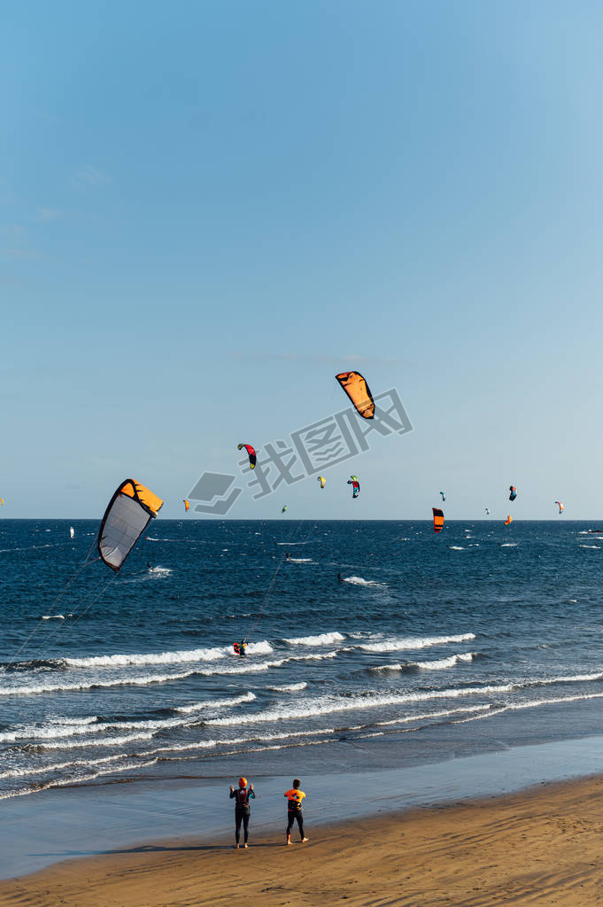 Many colorful kites on beach and kite surfers riding wes during windy day