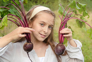 white girl of 10 years old holds 2 beets in her hands on a background of greenery