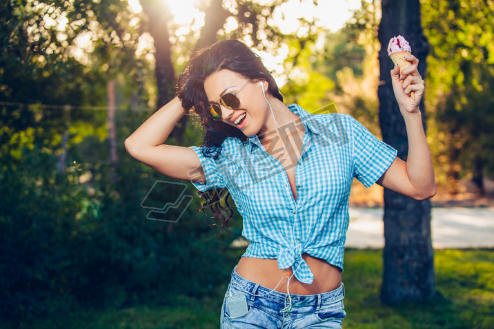 young beautiful short blue hair hipster woman with headphones music in the park. ice cream