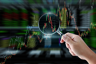 Hand holding magnifying glass with stock market graph background