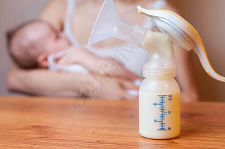 Manual breast pump with milk, mother and baby at background