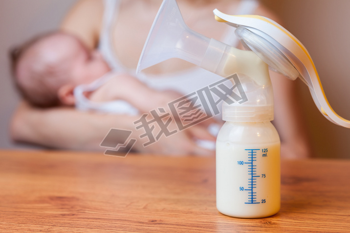 Manual breast pump with milk, mother and baby at background