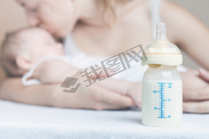 Baby bottle with breast milk and mother with baby