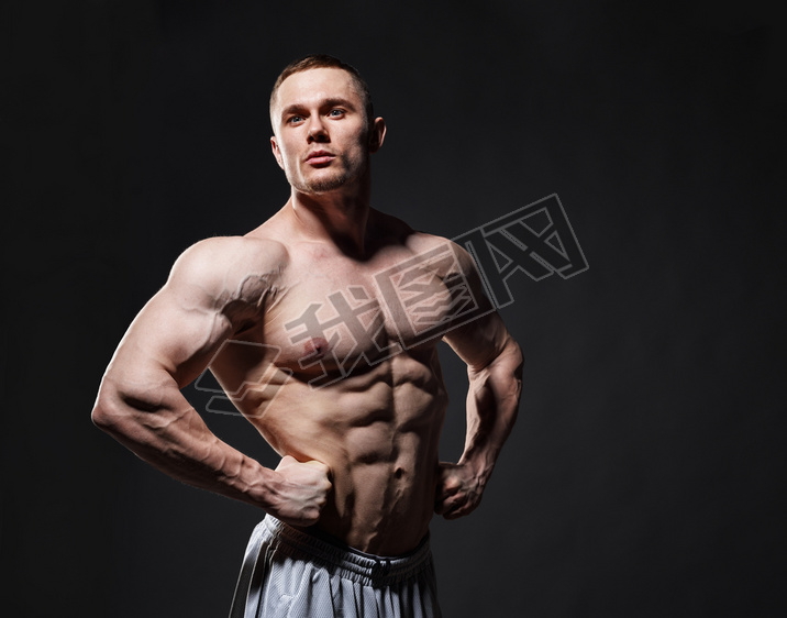 Strong muscular man posing in studio over dark background 