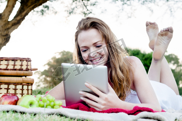 woman reads tablet lying on grass