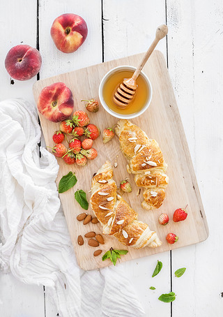 Freshly baked almond croissants with garden strawberries, peaches, mint and honey on serving board o