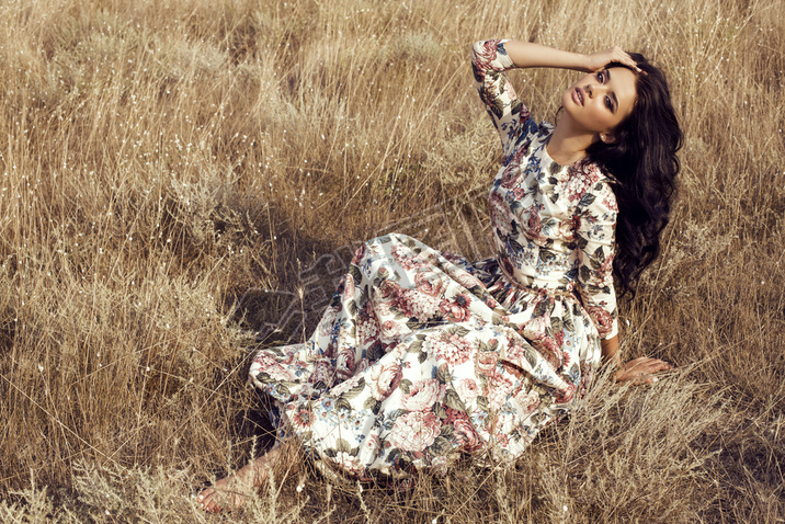 woman with dark hair wears luxurious colorful dress posing in summer field