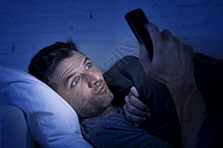 man in bed couch at home late at night using mobile phone in low