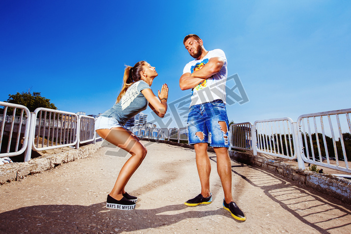 Young attractive girl is asking her man for forgiving making common gesture at summer bright backgro