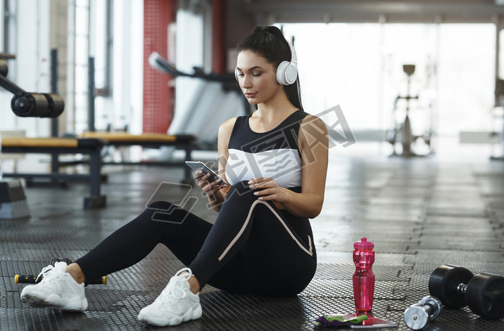 Young girl with headphones listening to music from artphone in gym