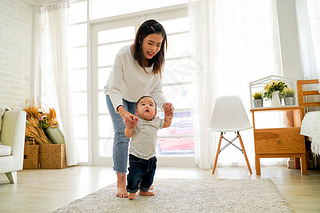 Asian mother encouraging and helping her cute son learn to walk his first steps