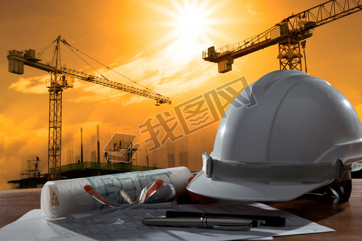 Safety helmet and architect pland on wood table with sunset scen