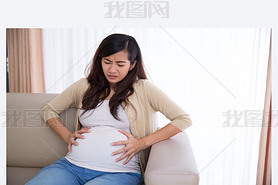 Asian pregnant woman has stomachache sitting on her couch