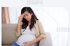 Pregnant asian woman got headache, sitting on a couch