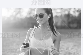 Black and white Athlete woman listening music looking at artphone after workout in nature outdoors