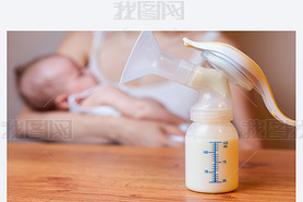 Manual breast pump with milk, mother and baby at background