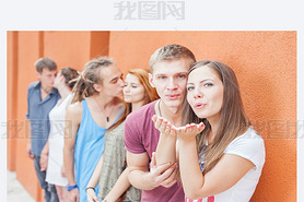 Group of happy young people standing near wall and kissing