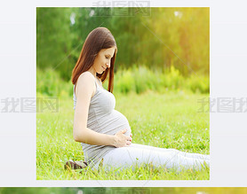 Portrait of happy pregnant woman sitting on the grass enjoys sun