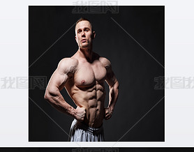 Strong muscular man posing in studio over dark background 