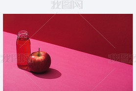 fresh juice in bottle near apple on red and pink background
