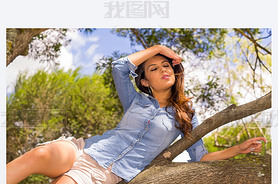 Pretty brunette model in park environment posing for camera lying on a tree holding her hair