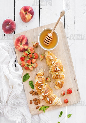 Freshly baked almond croissants with garden strawberries, peaches, mint and honey on serving board o