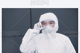 asian epidemiologist in hazmat suit and respirator mask looking at camera while standing outside and