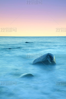 在安静的早晨在海上的浪漫气氛。从平静的波浪大海中伸出的巨砾。粉红色的地平线 