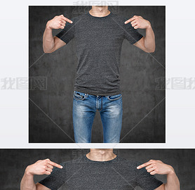 Close-up of a man pointing his fingers on a blank grey t-shirt. Dark concrete background.