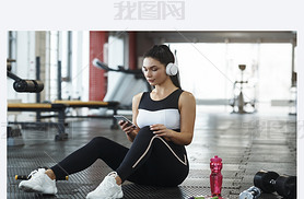 Young girl with headphones listening to music from artphone in gym