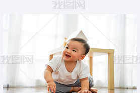 One lovely male infant laughing and hing fun in living room against white windows. He can sit on t