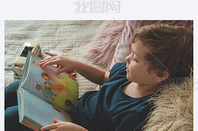 A little boy sits on a bed with your toys in living room watching pictures in story book