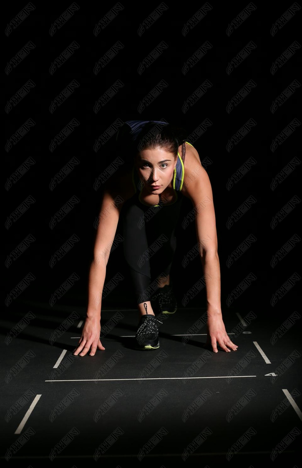 Athletic woman in position ready to run on black background.