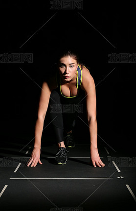 Athletic woman in position ready to run on black background.