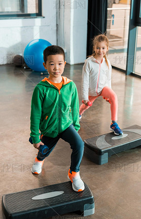 High angle view of multiethnic children holding dumbbells and working out on step platforms in gym