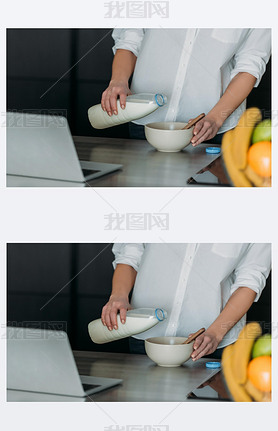 cropped view of woman pouring milk into bowl near laptop in kitchen