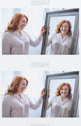 beautiful iling mature woman standing near mirror and looking at reflection