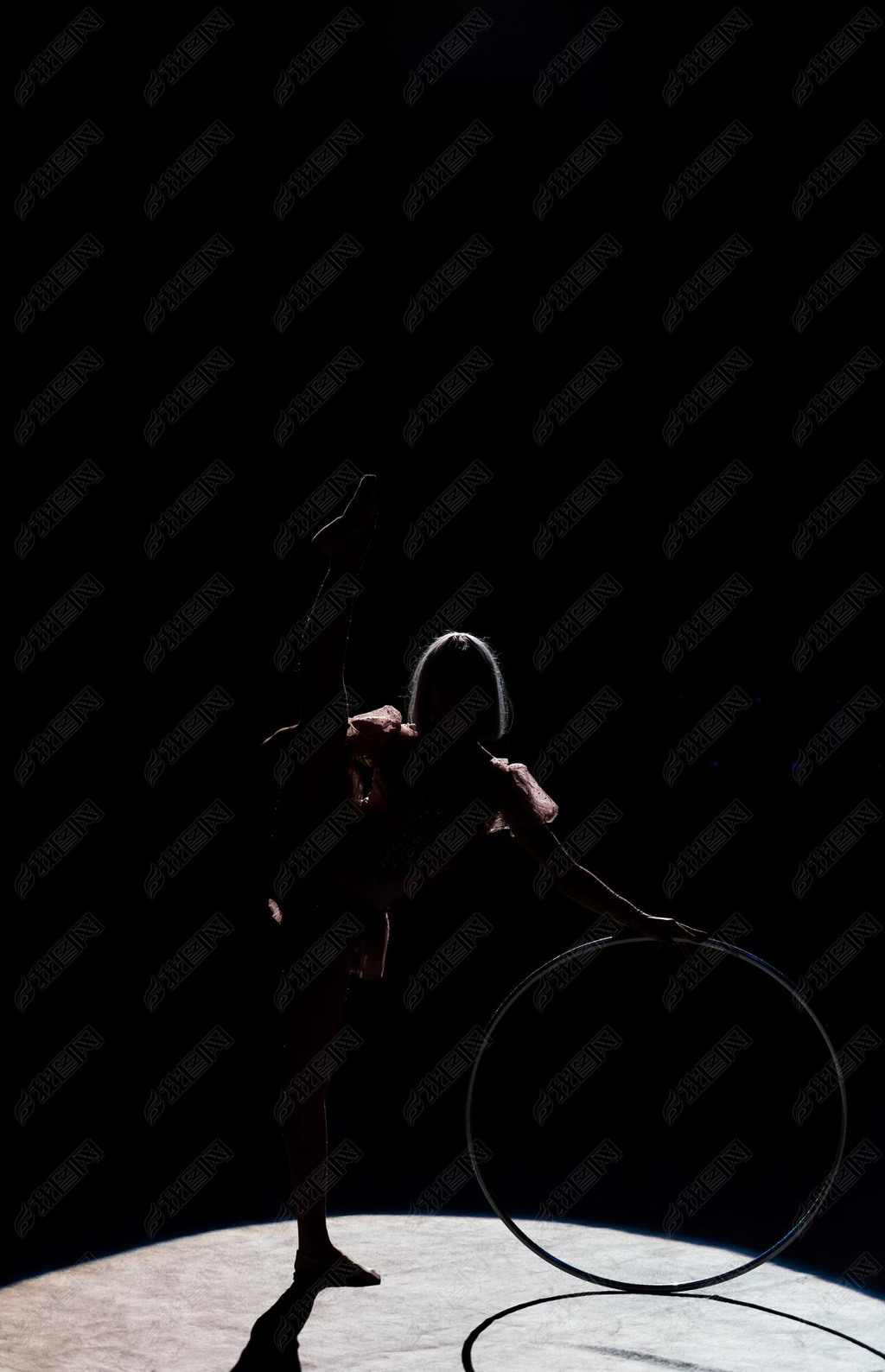 silhouette of flexible acrobat standing with hula hoop in arena of circus 