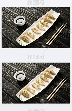 delicious Chinese boiled dumplings on plate near chopsticks and soy sauce on black wooden table