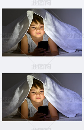 Little child play on art phone in bed under the covers at nigh